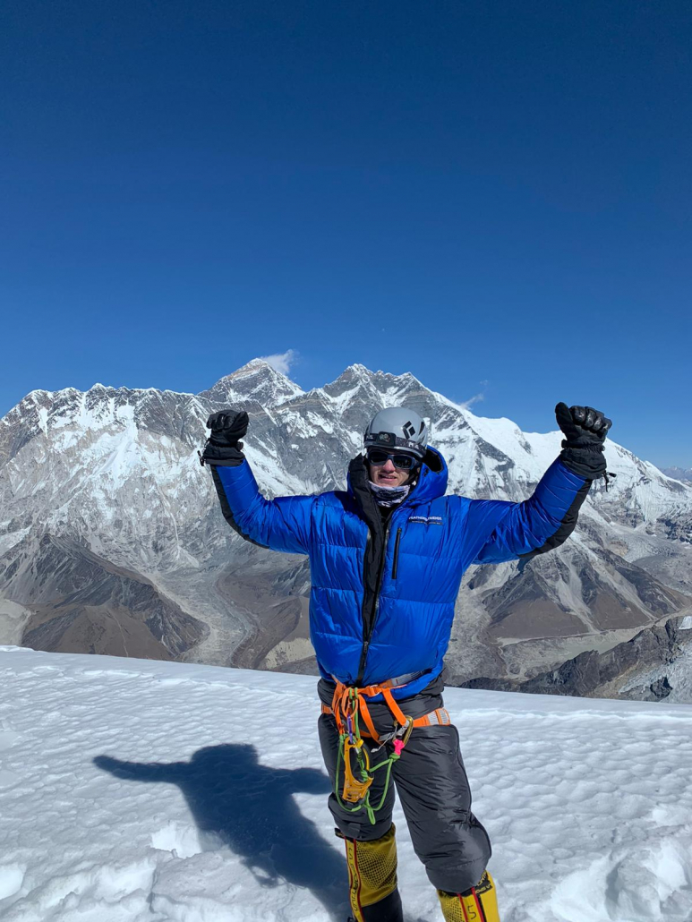 Chase M. on the summit of Ama Dablam with Everest and Lhotse in the background