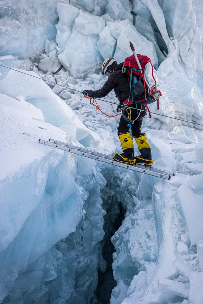 Climber Carter Beck crossing a ladder in the icefall