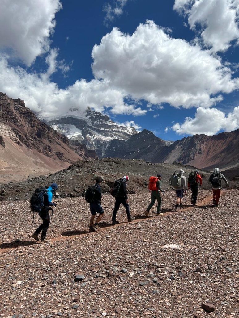 The team trekking toward base camp with Aconcagua in the clouds behind.
